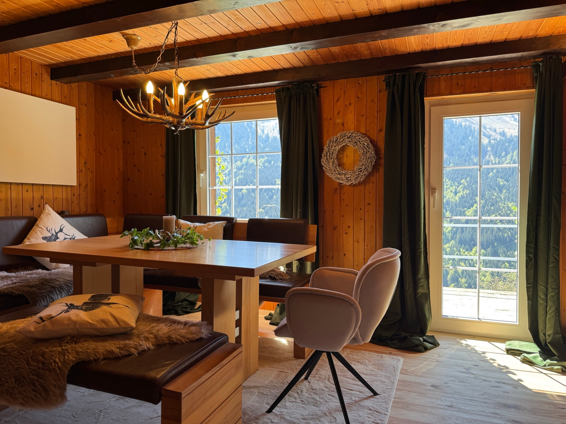 Dining area with wooden table, antler chandelier and terrace door with mountain views