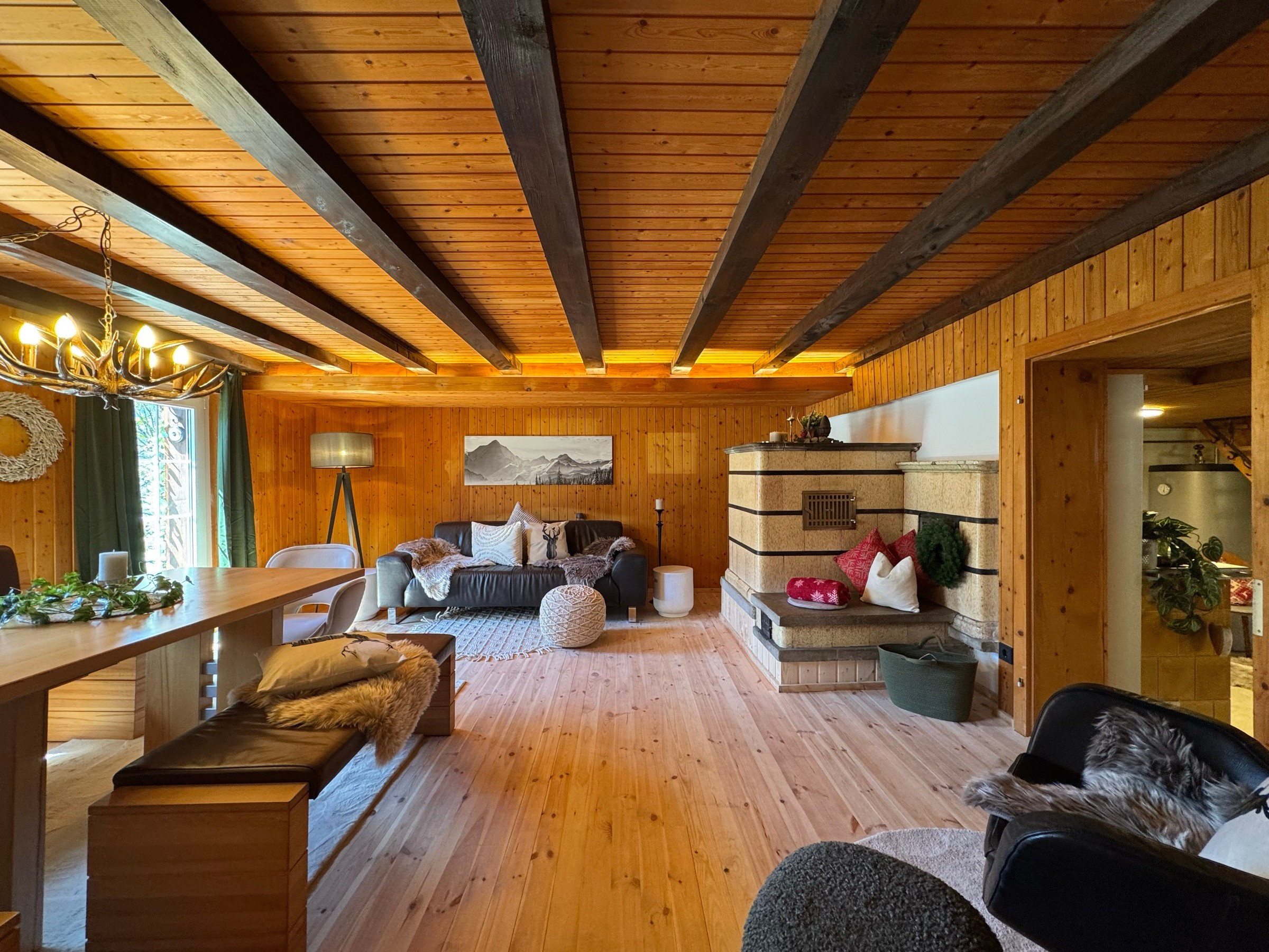 Living room with wooden beamed ceiling, tiled stove, leather sofa and large dining table